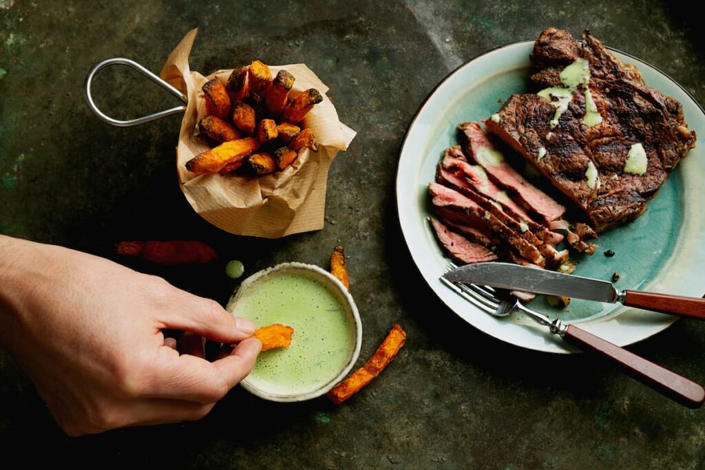 Imagem mostra bife de costela servido com batata crocante e molho.