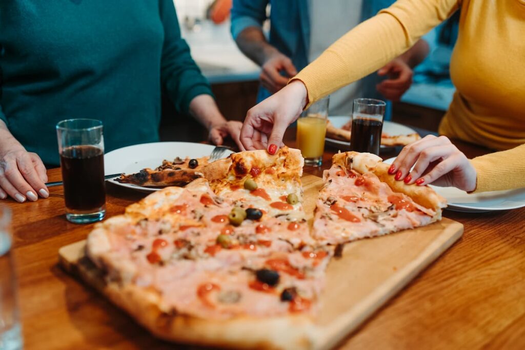 Imagem mostra pessoas comendo pizzas com azeitona.