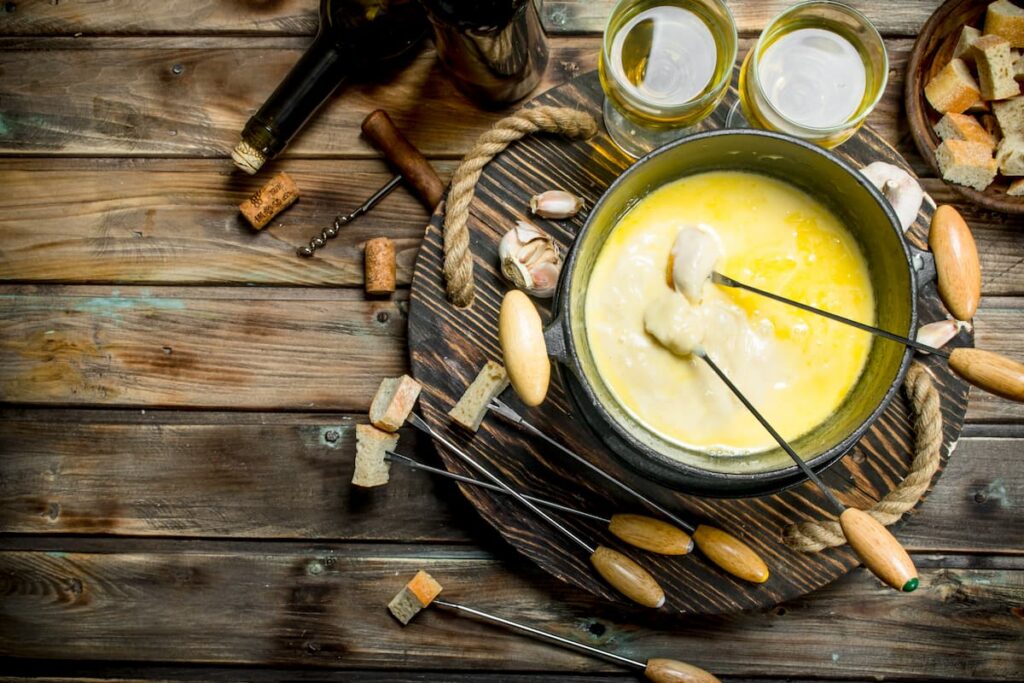 Imagem mostra um saboroso queijo fondue com azeitona e vinho branco.

