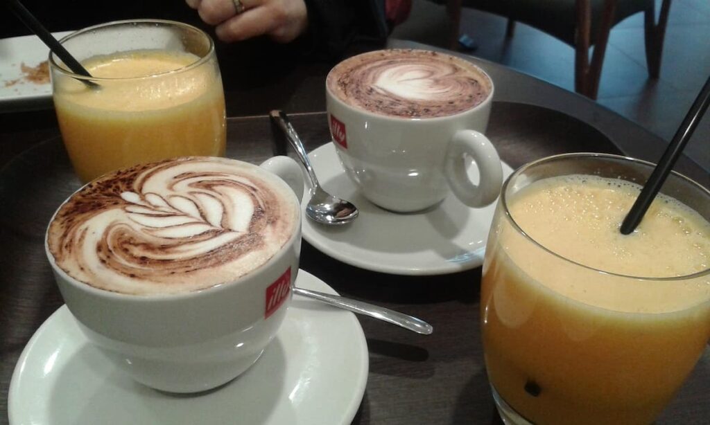 Imagem mostra mesa de café da manhã com capuccino e suco refrescante.