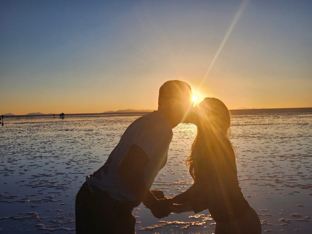 Imagem mostra casal curtindo o pôr do sol no Salar de Uyuni, na Bolívia.