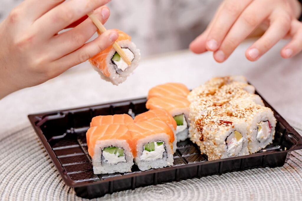 Imagem mostra jovem comendo suhi em restaurante japonês.